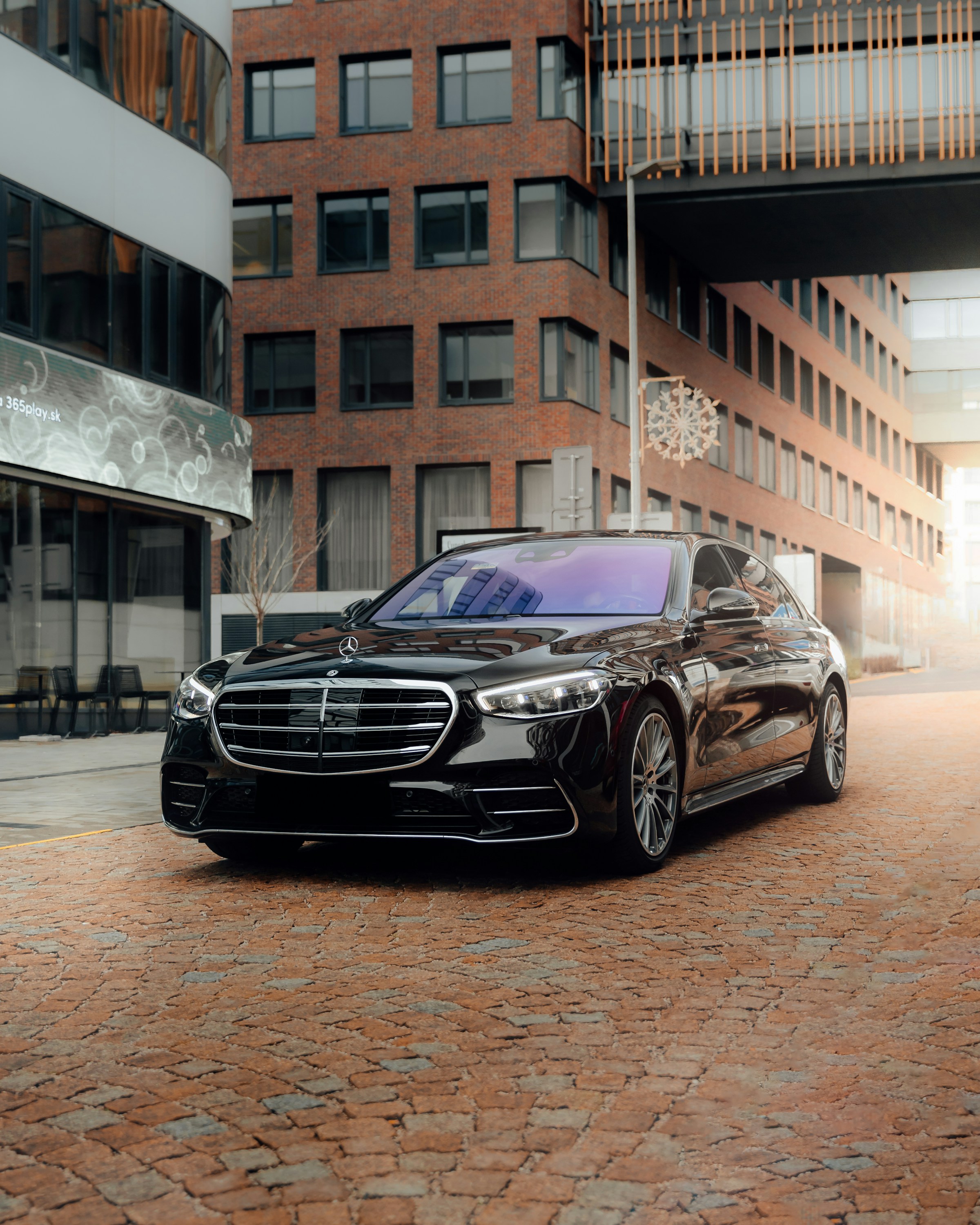 A black Mercedes-Benz S-Class on a sunlit cobblestone street